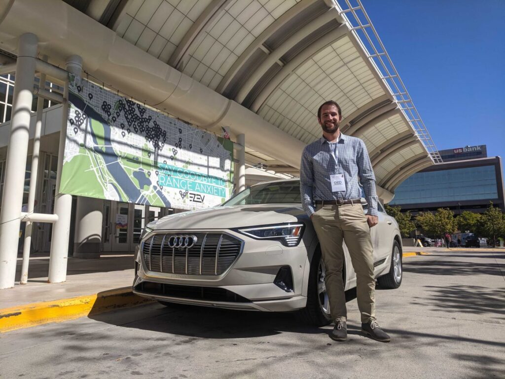 Person standing next to Audi electric vehicle in front of trade show venue